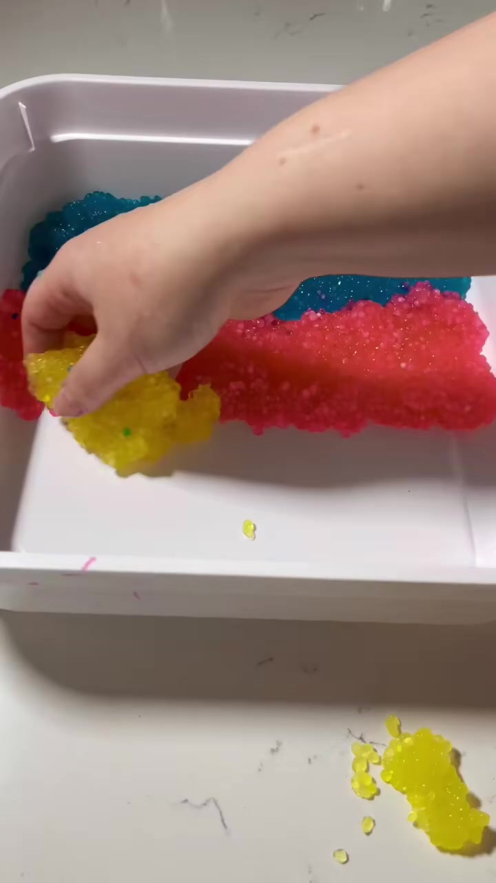 rainbow colored tapioca pearls in sensory bin stripes of color blue red yellow