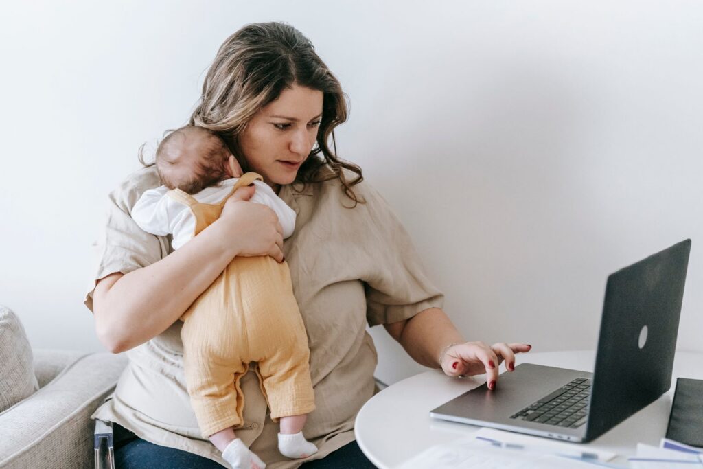 Mom holding her baby while typing on a laptop at home